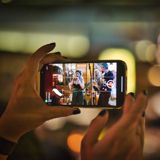 Nahaufnahme Musikfestival Em Bebbi sy Jazz: Frauenhände halten ein Smartphone und fotografieren die Szene, Musikerin auf der Bühne